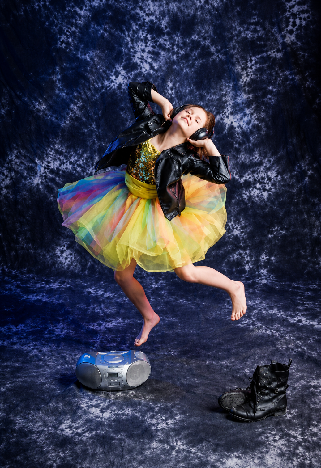 Oxbow Dance student in a rainbow tutu and leather jacket leaping with headphones on
